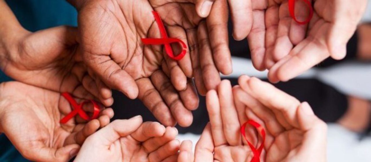 Many open hands held together, several holding small red HIV-awareness ribbons.