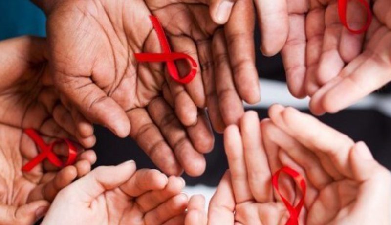 Many open hands held together, several holding small red HIV-awareness ribbons.