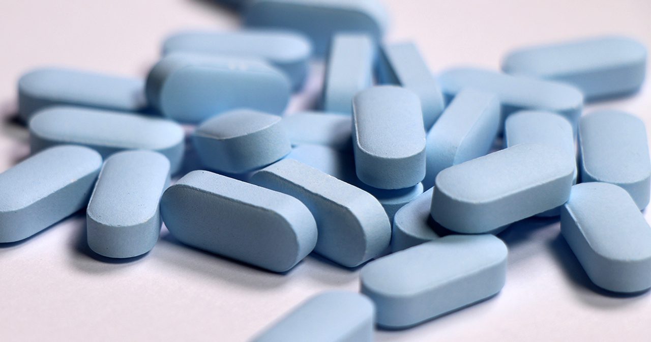 Close-up of a pile of blue PrEP pills on a white surface.