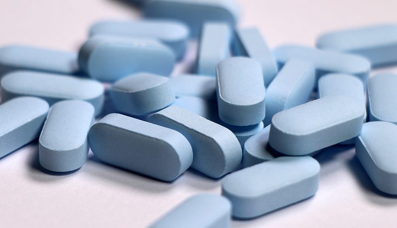Close-up of a pile of blue PrEP pills on a white surface.