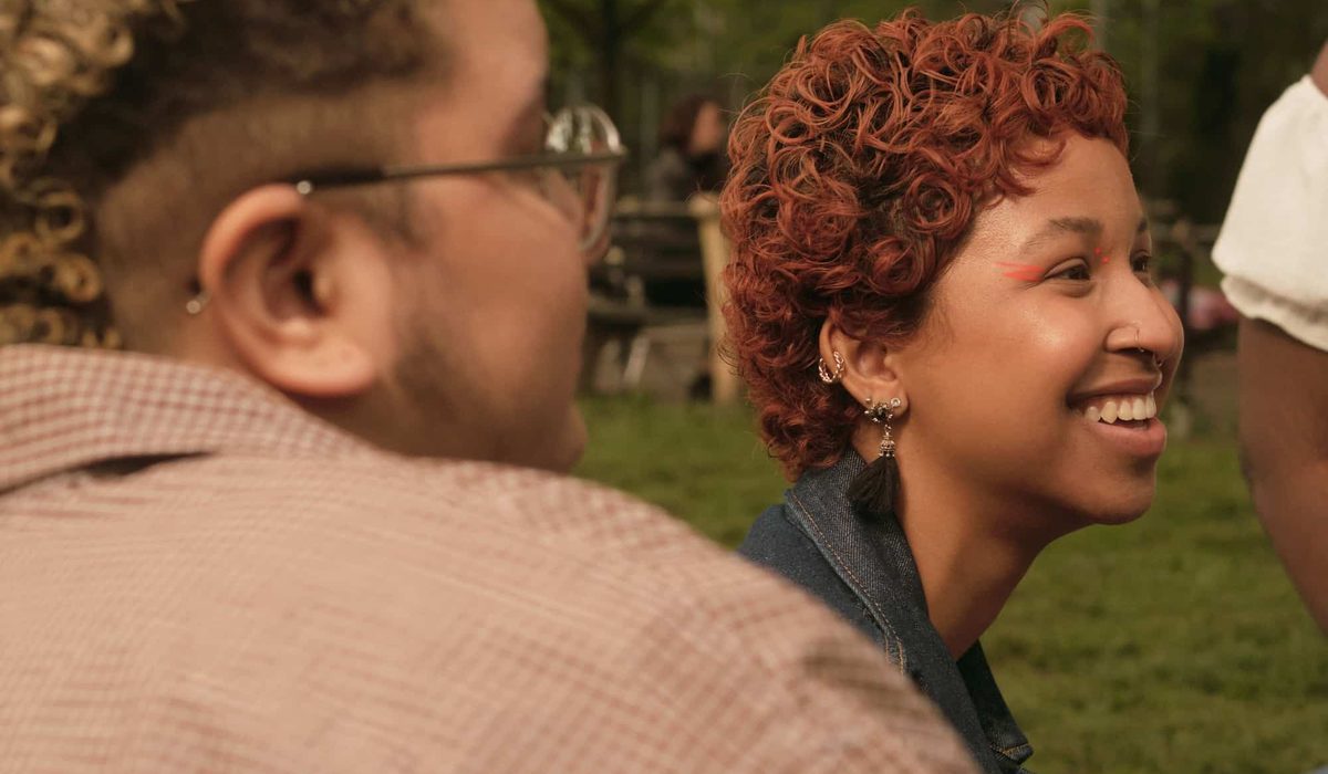 Two people sat in a park smile at something offscreen