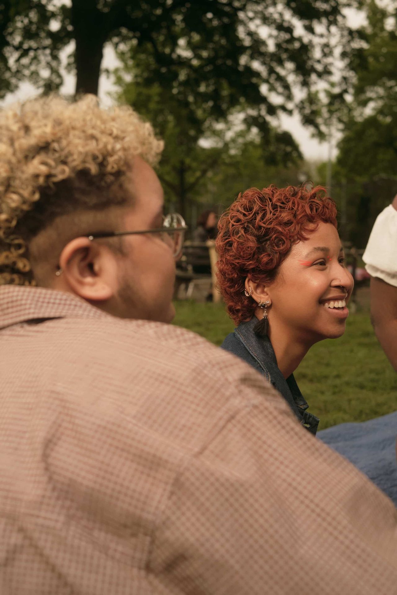 Two people sat in a park smile at something offscreen