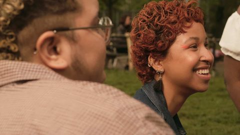 Two people sat in a park smile at something offscreen