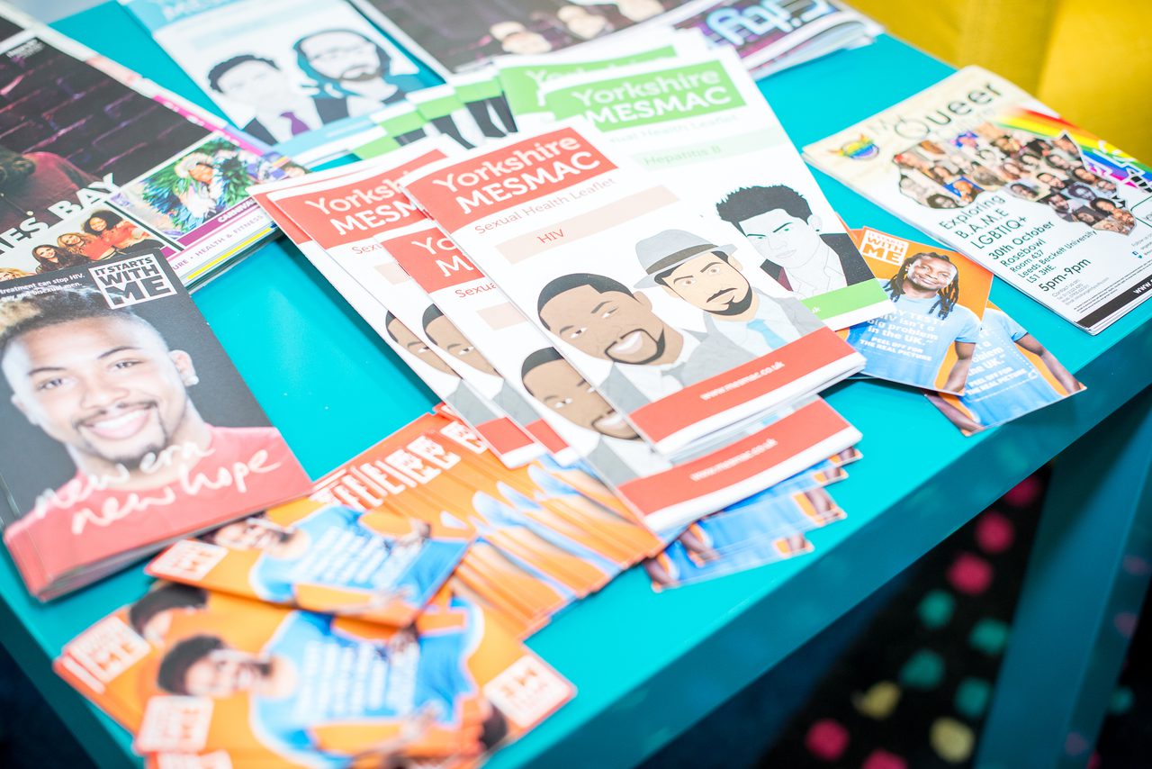 A teal table spread with Yorkshire MESMAC sexual health leaflets on HIV and Hepatitis B, a "Queer" LGBTIQ+ event flyer and other health booklets.
