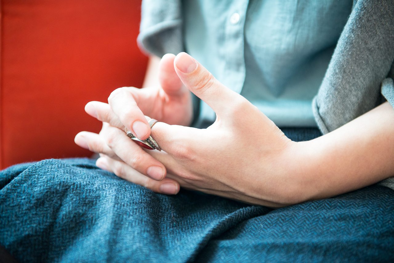 Close-up of a person's hands, one wearing a ring, resting on a blue lap against a red sofa.