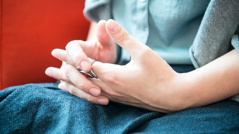 Close-up of a person's hands, one wearing a ring, resting on a blue lap against a red sofa.