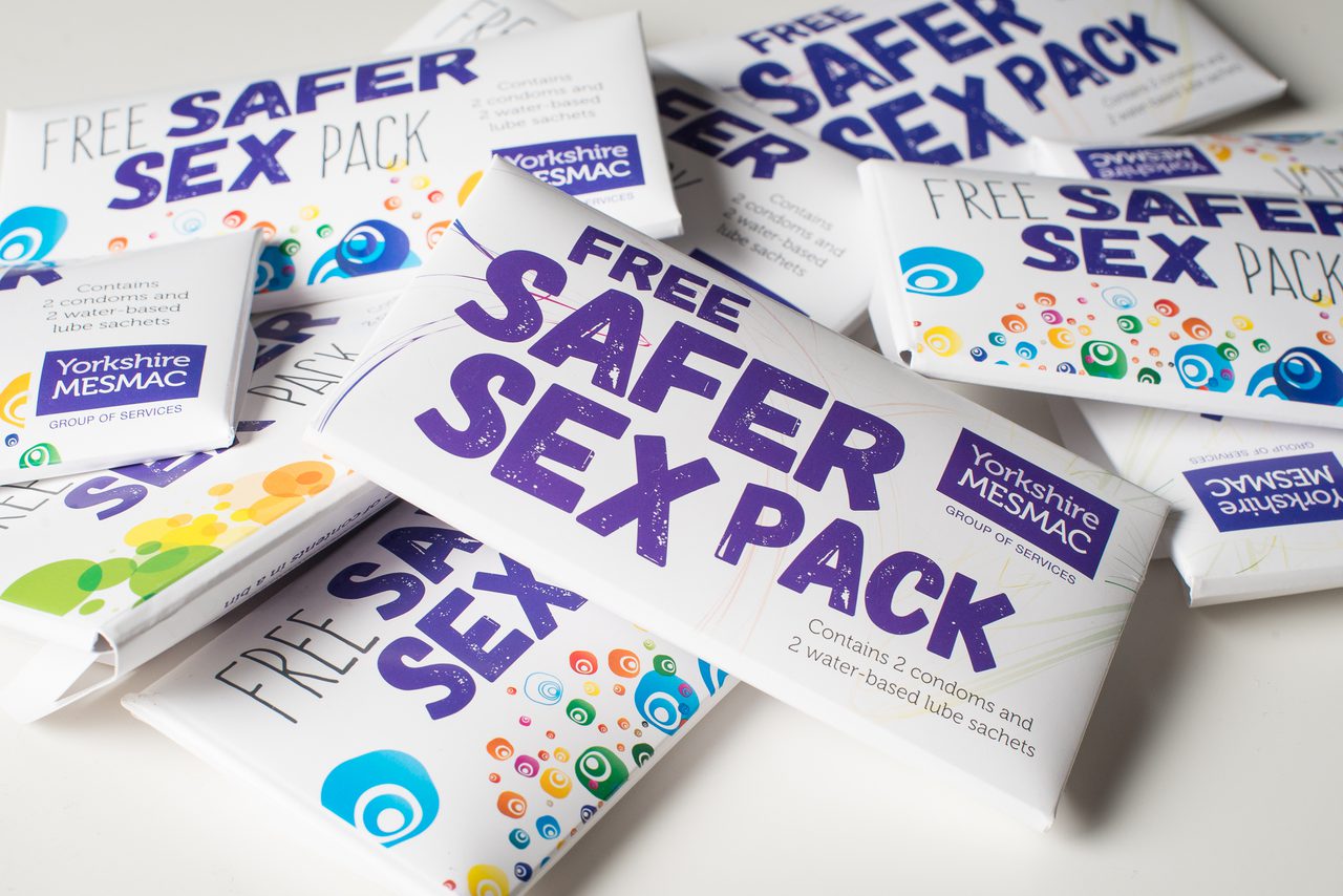 A pile of safer sex packs. The text on the cardboard envelopes reads: Free Safer Sex Pack. Yorkshire MESMAC. Contains 2 condoms and 2 water-based lube sachets
