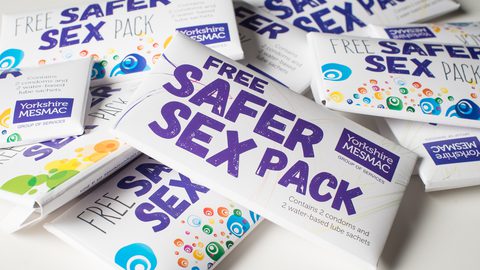 A pile of safer sex packs. The text on the cardboard envelopes reads: Free Safer Sex Pack. Yorkshire MESMAC. Contains 2 condoms and 2 water-based lube sachets