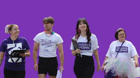 Four people walking together in Yorkshire MESMAC t-shirts against a purple background, some wearing Pride accessories and a tutu.