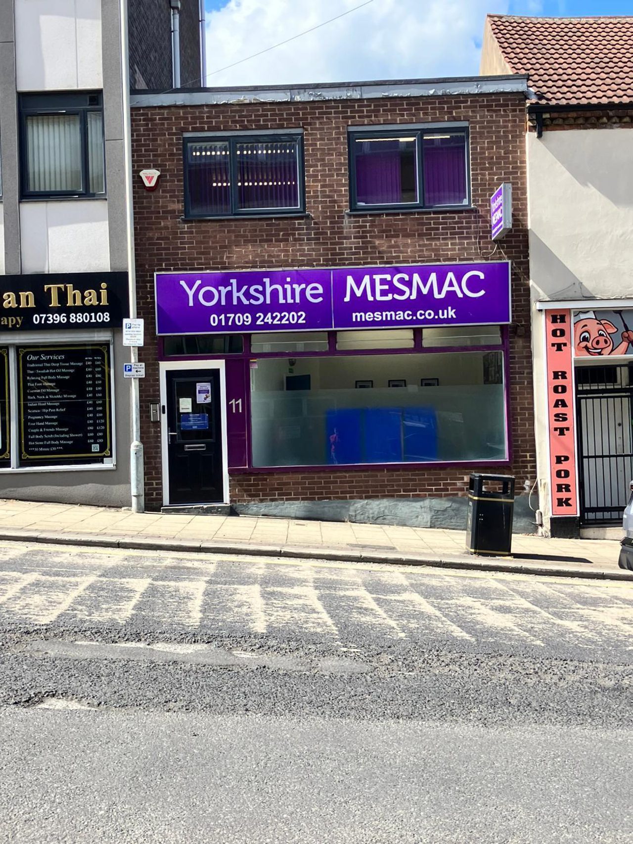 The Yorkshire MESMAC Rotherham office shopfront, a brick building with a purple "Yorkshire MESMAC" sign and a numbered door, on a sloping street beside a roast-pork shop.
