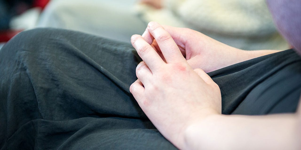 Close-up of a person's hand resting on their lap in dark clothing after a finger-prick test.