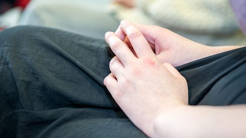 Close-up of a person's hand resting on their lap in dark clothing after a finger-prick test.