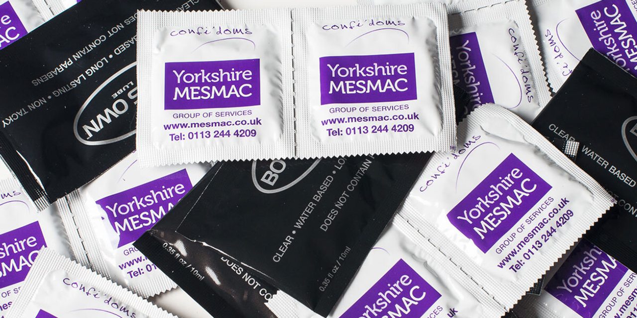 A pile of Yorkshire MESMAC condom sachets and black water-based lube sachets.