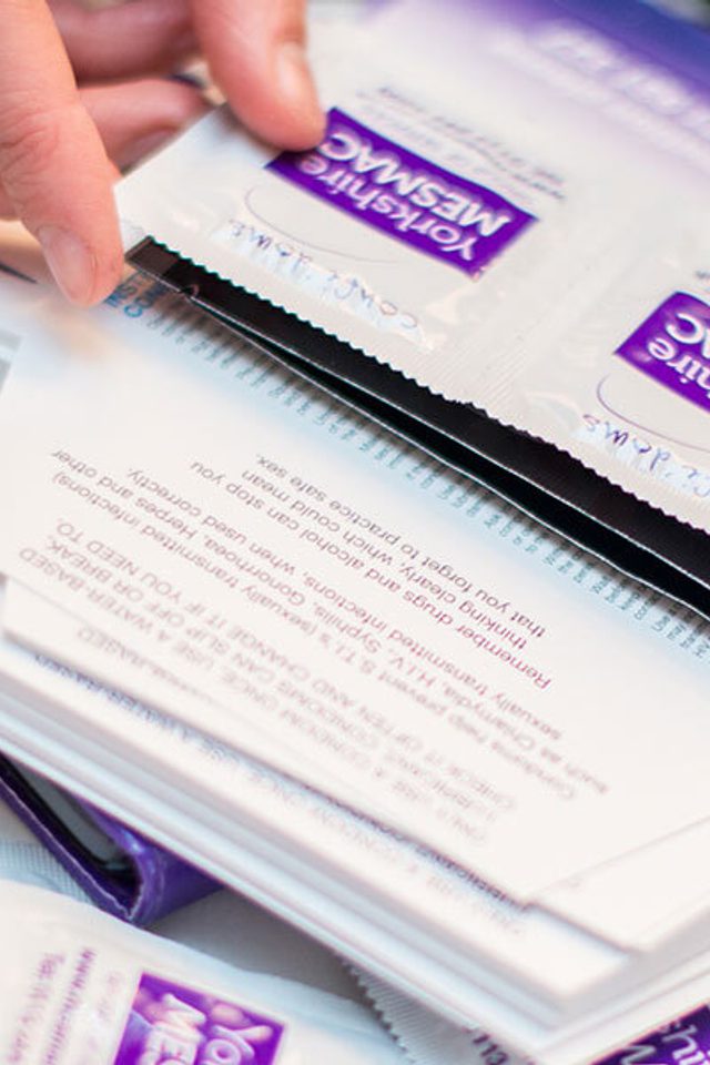 Close-up of hands sorting through a pile of Yorkshire MESMAC condom packets on a table.