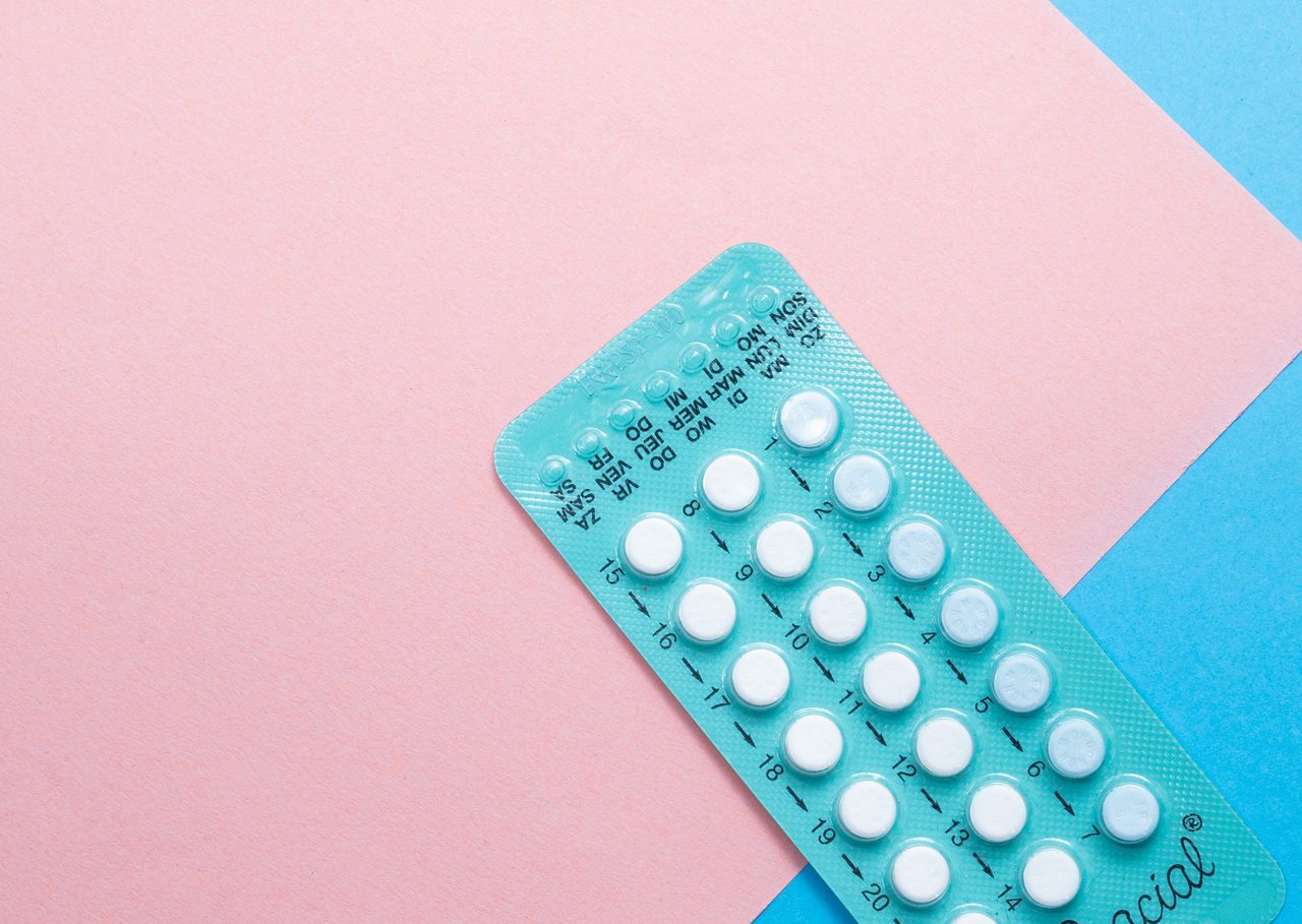 A contraceptive pill blister strip on a pink and blue background.