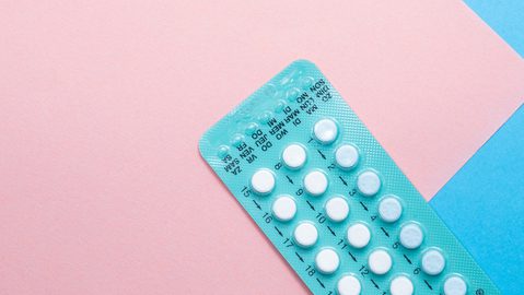 A contraceptive pill blister strip on a pink and blue background.