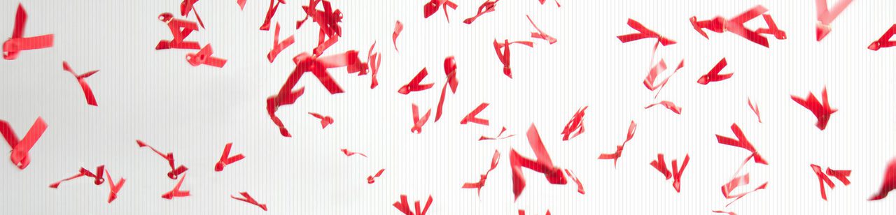 Red HIV-awareness ribbons scattered and falling against a white background.