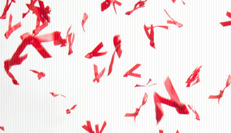 Red HIV-awareness ribbons scattered and falling against a white background.