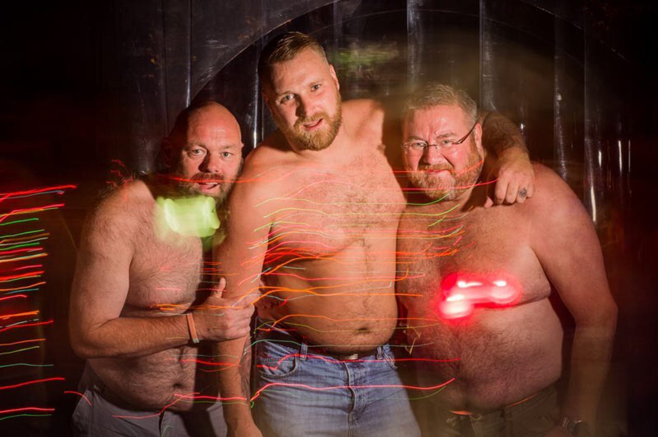 Three people posing together, smiling, at a nighttime event lit with colourful light trails.